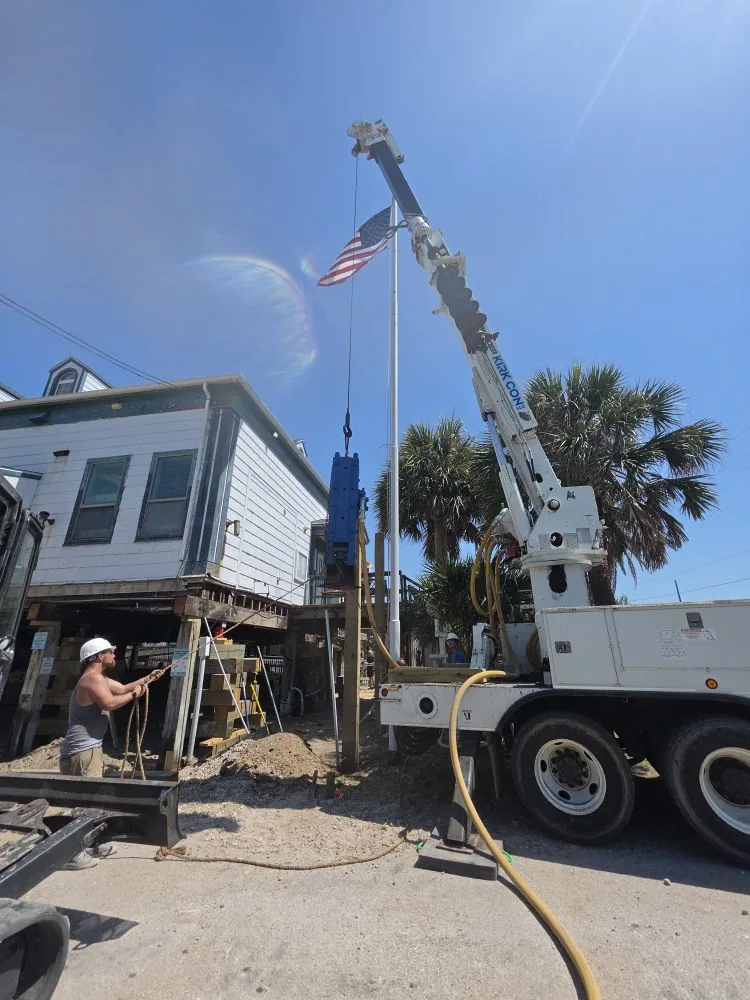 Kirk Con LLC crew member guiding a timber pile beside an elevated beach house
