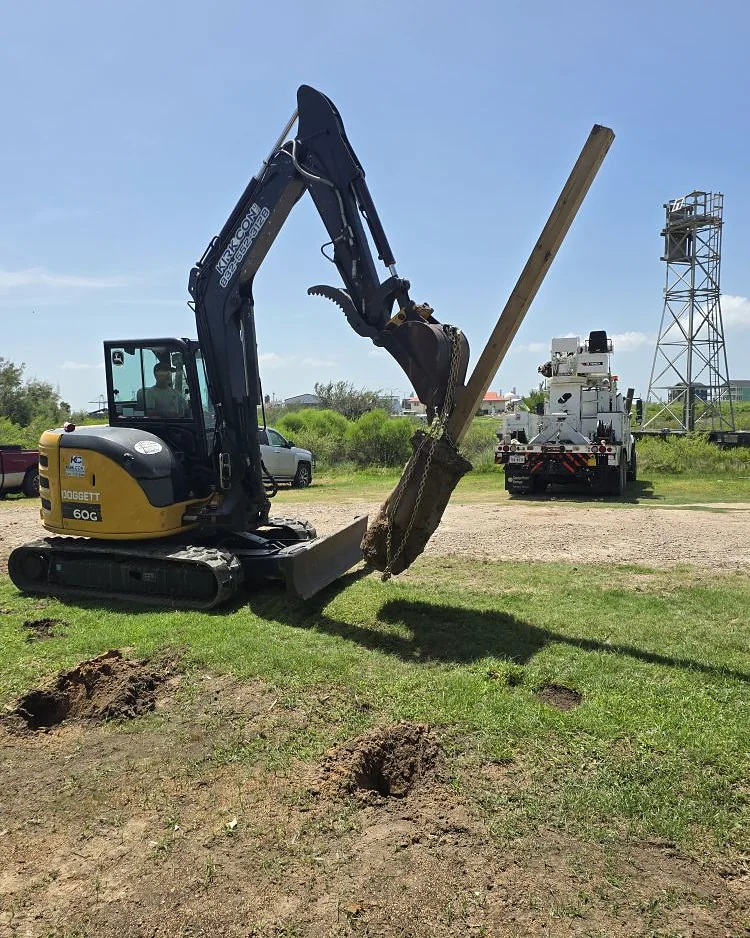 Kirk Con LLC excavator setting a timber pile upright before driving