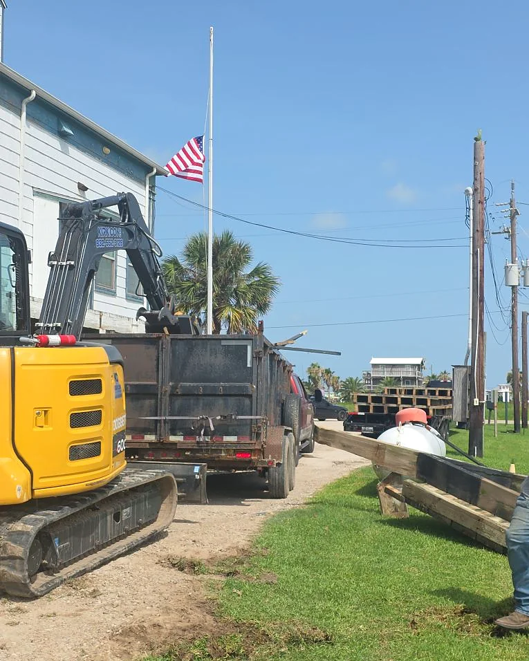 Excavator, dump trailer and timber pilings staged for a coastal piling installation