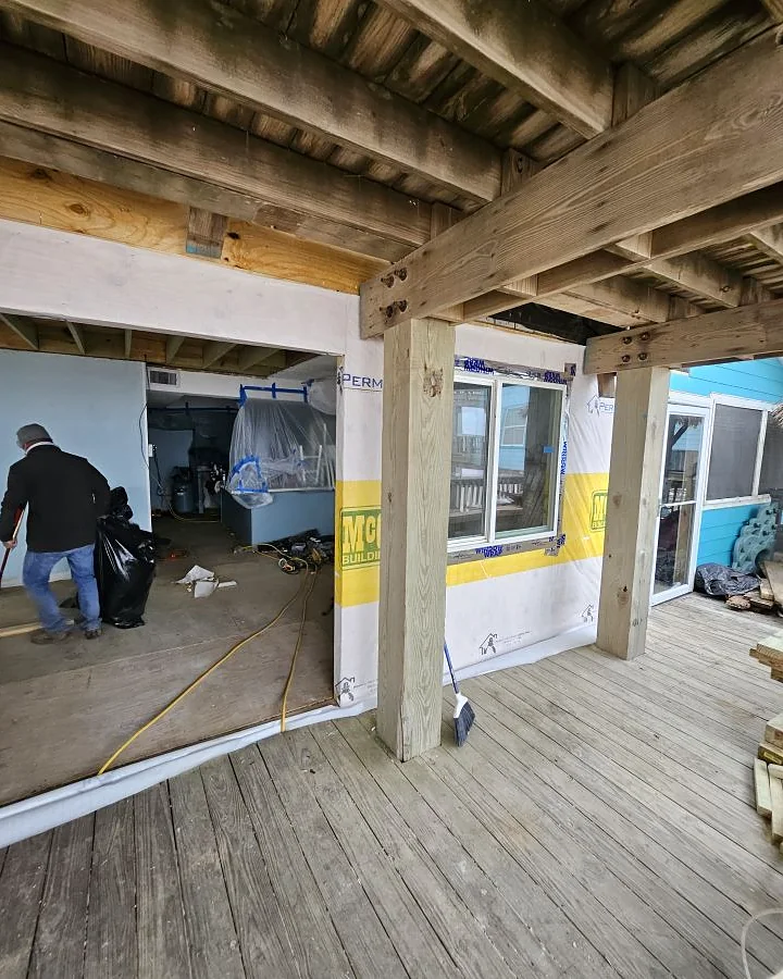 Kirk Con LLC crew working beneath an elevated coastal home during a window and weather barrier install