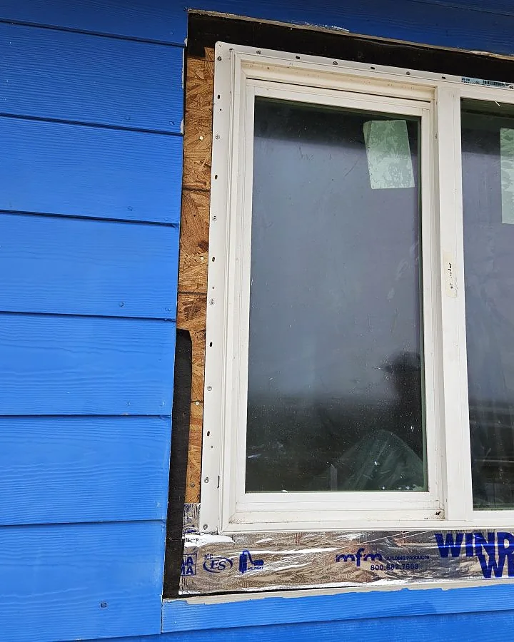 Newly installed window trimmed into blue lap siding on a coastal home exterior